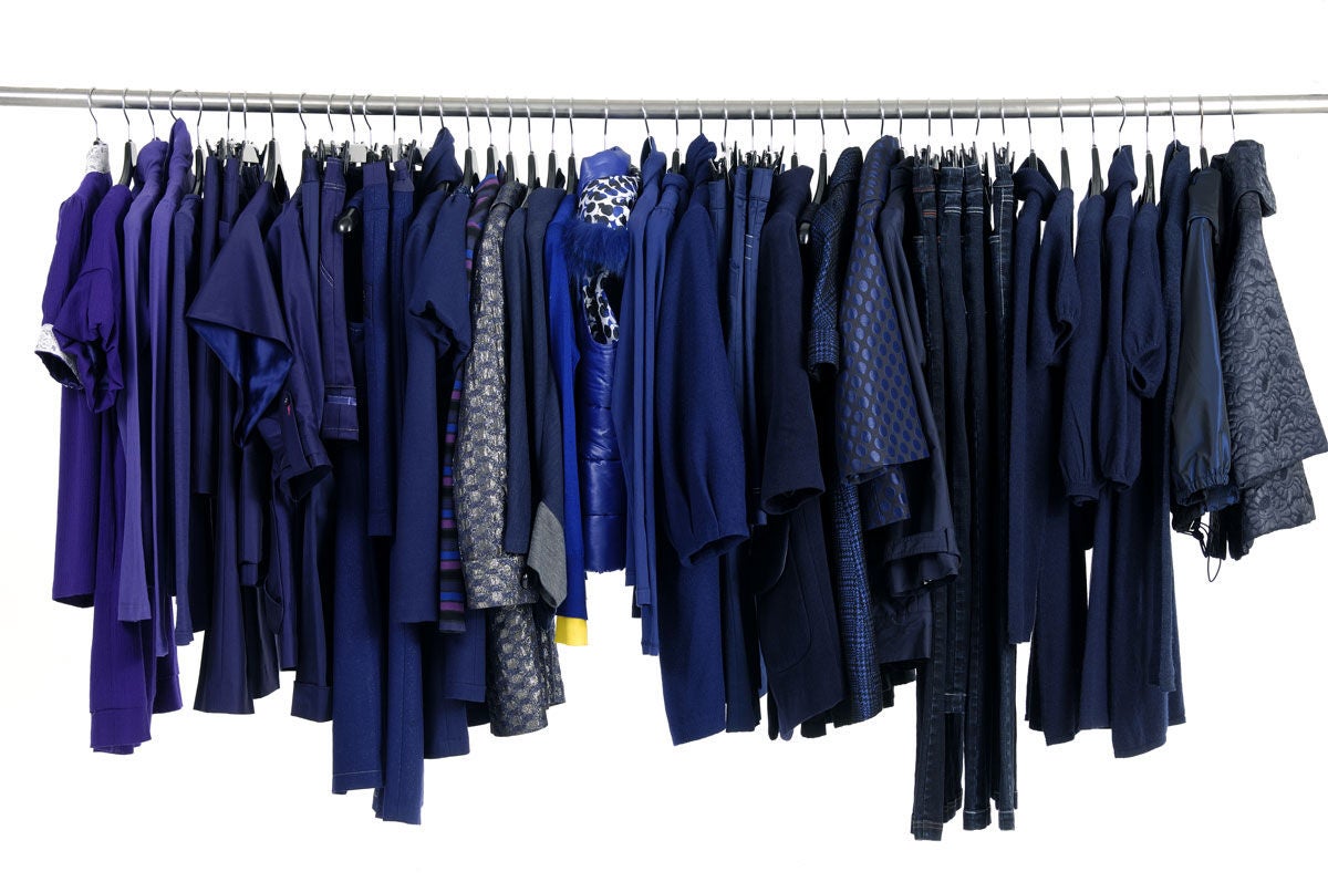A row of various dark-coloured clothing items, including shirts, jackets, and pants, hanging neatly on metal hangers along a clothing rack.